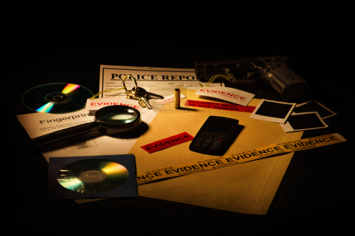Fictious police desk with crime case records containing gun, blank photos, crime scene information sheet, cd roms, magnifying glass, keys, mobile phone, bullet shell and police reports.