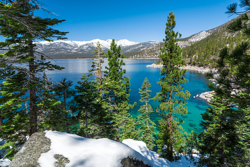 Picture of Lake Tahoe in early spring of 2015 with view on snowy peaks of Sierra Nevada mountains. There is snow on the rocks in Tahoe forest.