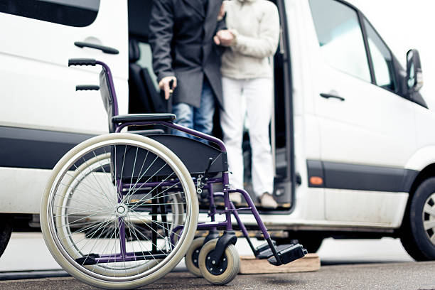 perawat membantu pria senior keluar dari van dan sampai ke kursi rodanya