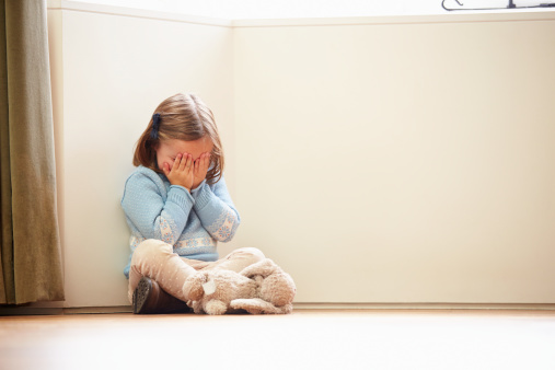 Unhappy Child Sitting On Floor In Corner Crying To Herself At Home