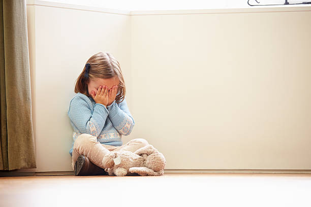 A girl sits at a corner, covering her face with her hands Unhappy Child Sitting On Floor In Corner Crying To Herself At Home child abuse stock pictures, royalty-free photos & images