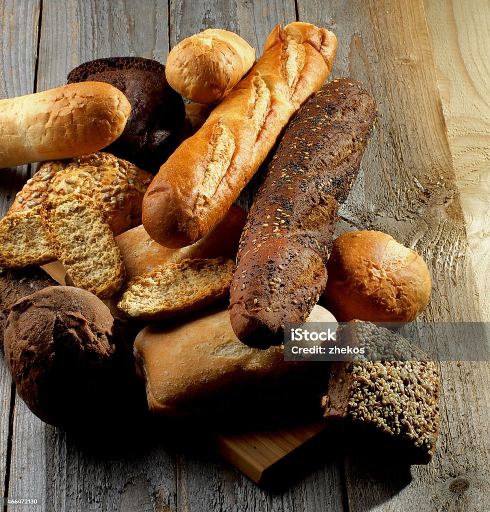 Various Bread Heap of Various Various Buns, Baguette, Poppy Seed and Sesame Buns, Rye and Whole Wheat Bread isolated on Rustic Hardwood background 2015 Stock Photo