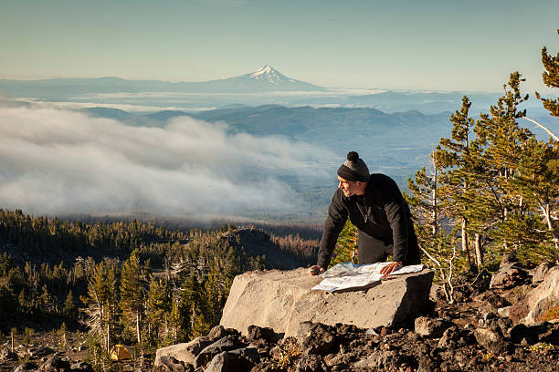 Navigating the Mountain A hiker / Climber consults a topo map on the side of Mount Adams, WA.  Mount Hood can be seen in the distance. orienteering stock pictures, royalty-free photos & images