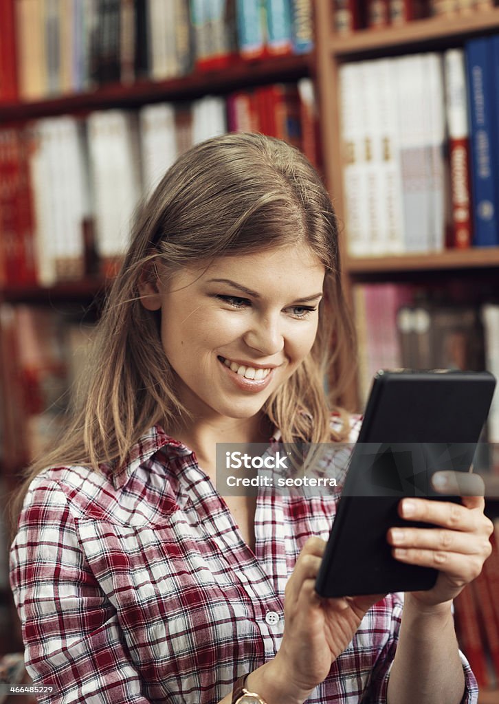 Book shop owner Young smiling female merchant with iPad tablet in book store or library. Happy successful commerce woman over books shelf background. Adult Stock Photo