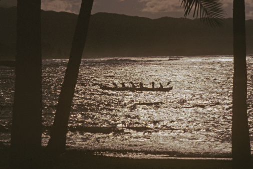 An outrigger canoe is shown racing on the Ali Wai Canal, Oahu at sundown