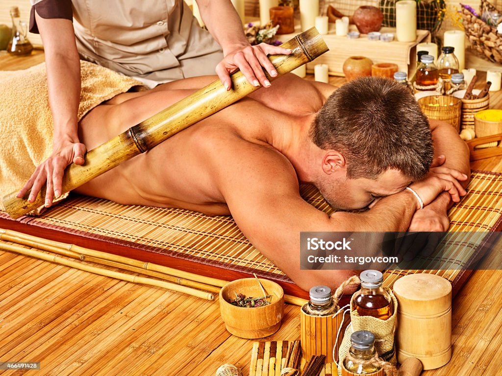 A man receiving a bamboo massage Man getting bamboo massage. Female hand  therapist.Wooden floor. Bamboo - Plant Stock Photo