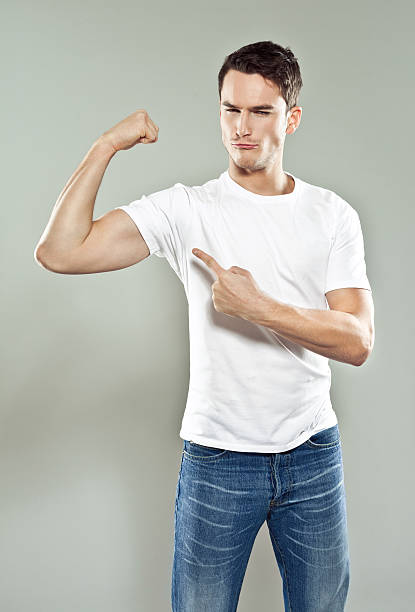 Flexing muscels Portrait of confident young man wearing white t-shirt flexing his bicep. Studio shot, gray background. young man wink stock pictures, royalty-free photos & images