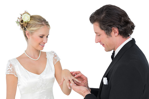 Attractive bride and groom exchanging wedding ring against white background