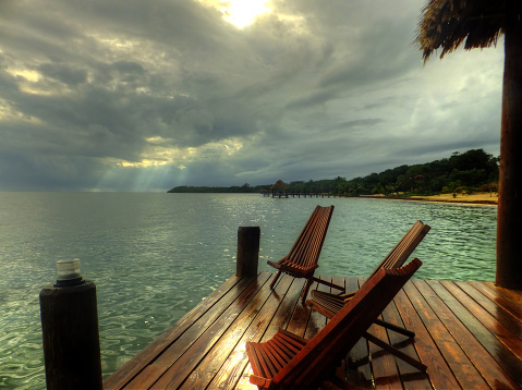 Empty chairs on a dock in Belize with storm clouds and sunbeams.