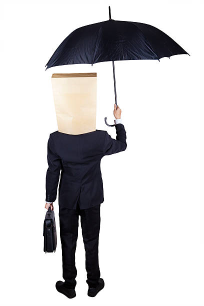 Rear view of entrepreneur with umbrella Businessman with cardboard head standing in the studio while holding umbrella with briefcase anonymous businessman with paper bag on his head stock pictures, royalty-free photos & images