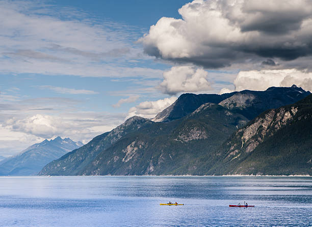 Kayakers in Southeast Alaska near Haines on a summer day with puffy clouds.