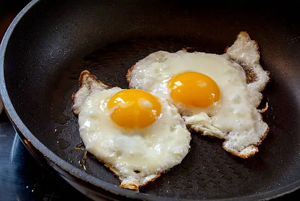 two fried eggs in a black pan, breakfast preparation