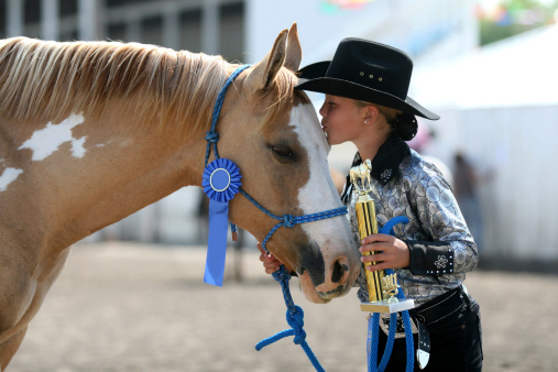 cowgirl contestant holding her ribbons she won with her horse in an arena during fair