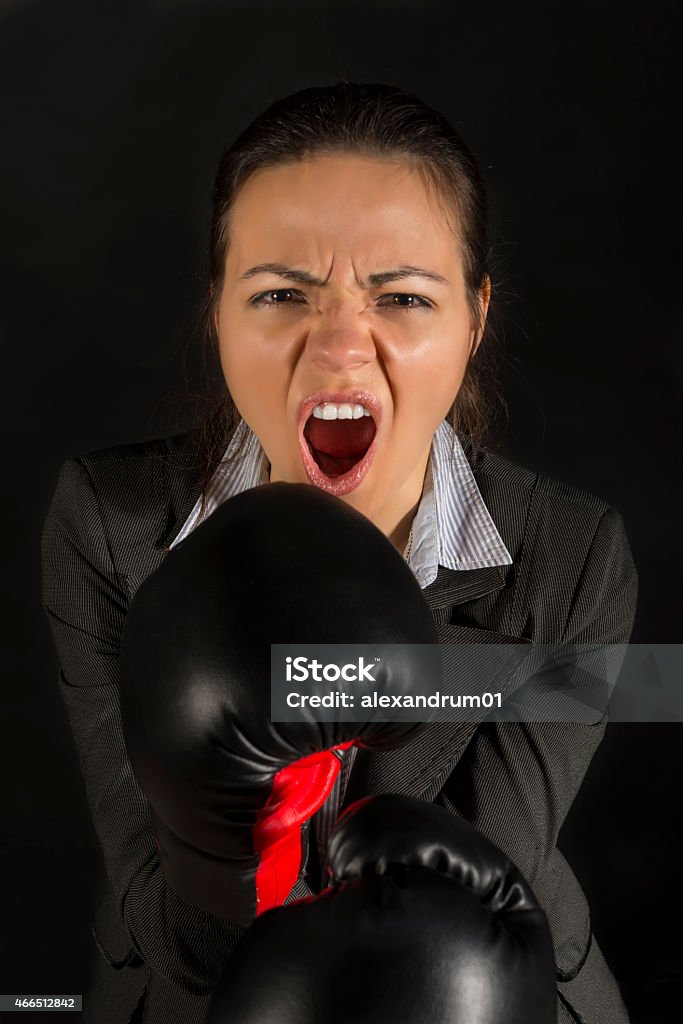 Woman screaming ready to fight Extremely furious business woman in attack with boxing gloves on black background Aggression Stock Photo