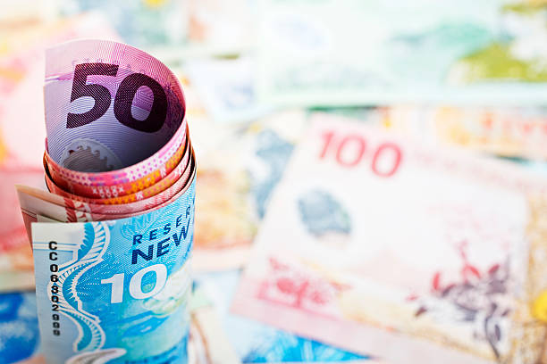 New Zealand Currency Roll and Background Rolled up New Zealand banknotes standing on an out of focus background of notes. new zealand dollar photos stock pictures, royalty-free photos & images