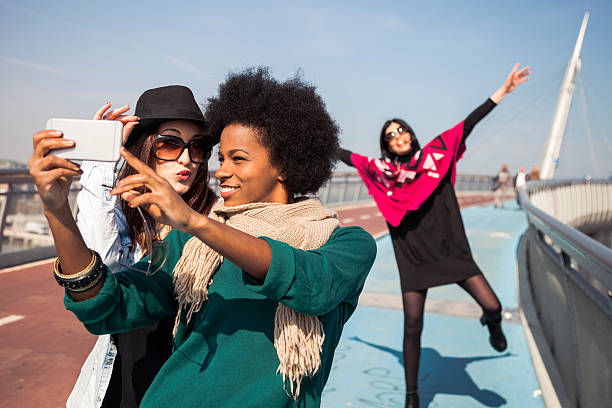 Two friends victim of "photo bombing" taking a selfie Two friends while taking a selfie on mobile phone are victim from another woman of "photo bombing". The photo bombing is when intentionally posing in other people's photos, for a later surprise. photo bomb stock pictures, royalty-free photos & images