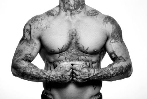 Bare chested man with religious tattoos and closed fists. Black and white torso against white background. Religious tattoos. Hand made tattoos.