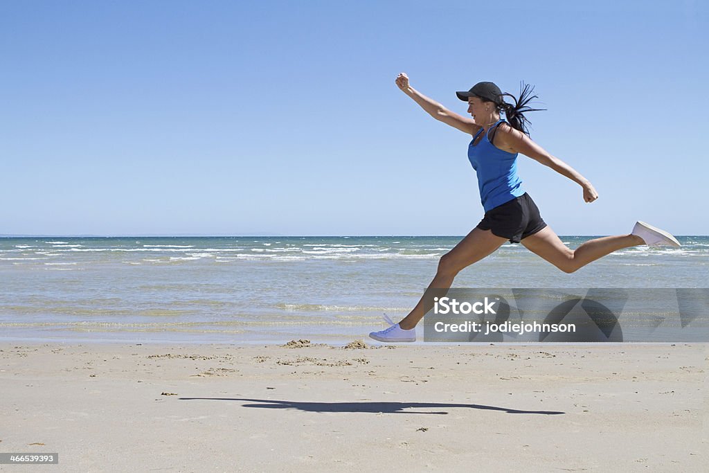 Fit woman leaping mid air on a beach Fit woman leaping mid air on the beach with ocean behind Active Lifestyle Stock Photo