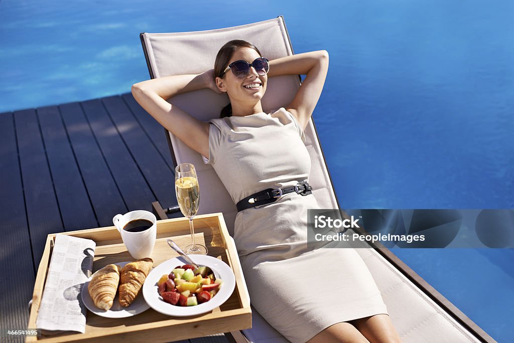 Poolside pampering An attractive young woman reclining on a deck chair with her food next to her Swimming Pool Stock Photo