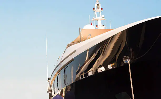 Closeup side view of black luxury yacht agains blue sky in sunlight with copy space