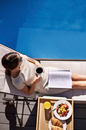 Top view of an attractive young woman enjoying her breakfast by the pool