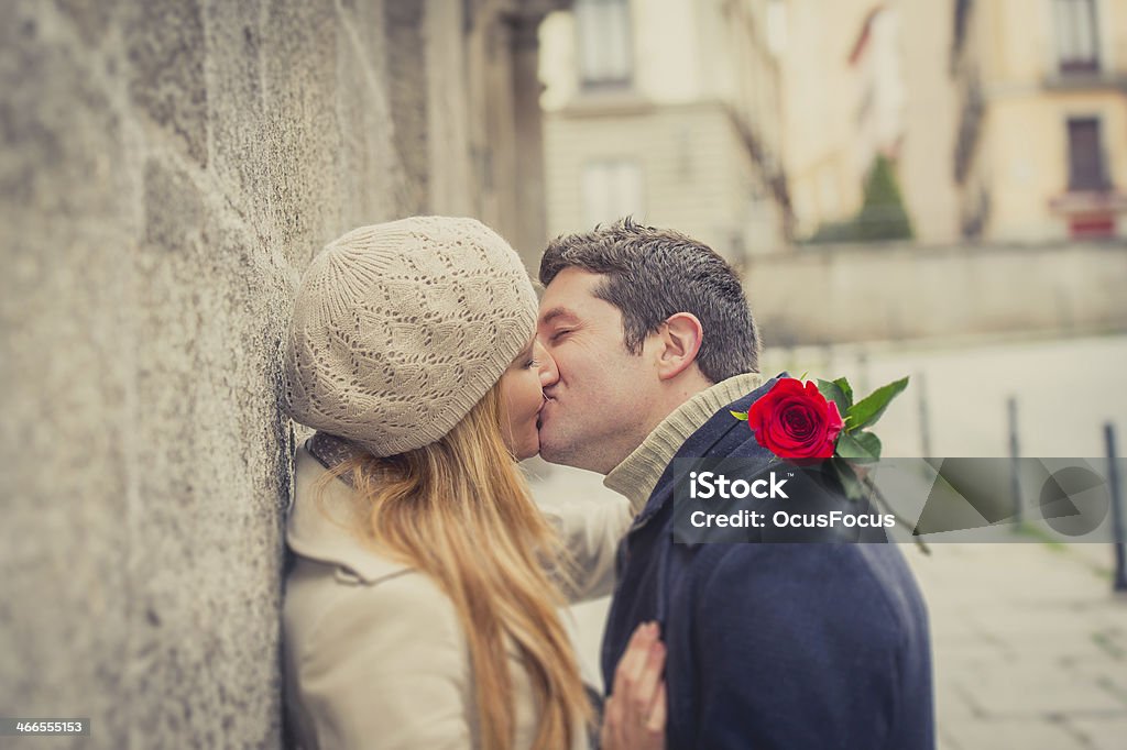 couple with a rose kissing on valentines day or anniversary young man giving his girlfriend a rose and kissing celebrating valentines day on urban winter clothes Couple - Relationship Stock Photo