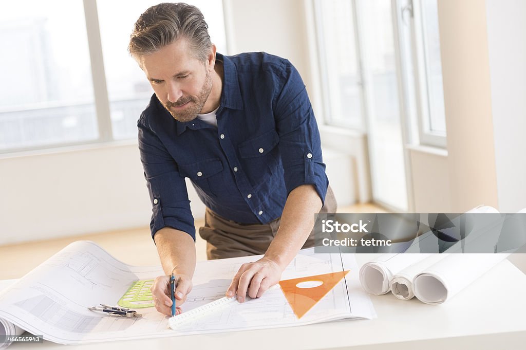 Architect Working On Blueprint At Office Desk Handsome mature male architect working on blueprint at office desk Architect Stock Photo