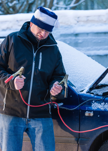 A man waits help with the booster cables beside the car, cold winter day