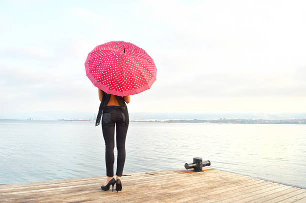 A woman wearing sexy jean and carrying a red umbrella walks on a pier