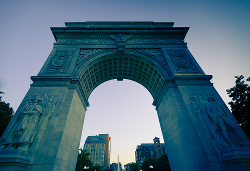 Looking up at the arch in Washington Square, New York City, which is lit up blue at dusk.