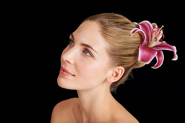 An attractive young woman with a flower in her hair against a black background