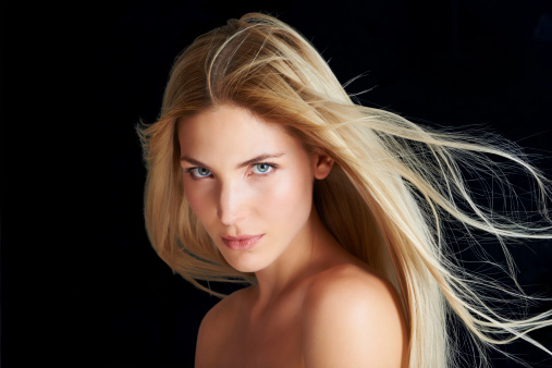 A beautiful young woman posing in front of a black background with the wind blowing through her hair