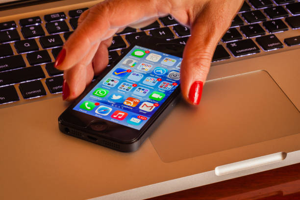 Bogota, Colombia - March 10, 2015: A latin lady picks up an Apple iPhone 5 from a computer keyboard. Her fingermails are painted brick red. Photo shot in the horizontal format with flash lighting only. The long exposure causes some motion blur; but the second curtain flash eventually freezes the fingers creating a sense of motion. Three flashes used to balance light. Focus on second and third rows row of icons from the bottom. Camera: Canon EOS 5D MII. Lens: Leica APO Summicron - R 90 mm f2 ASPH.