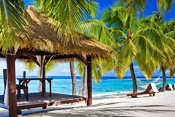 Tropical gazebo with chairs on deserted beach with palm trees