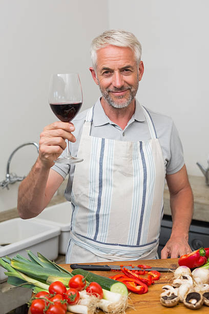 istock Mature man with wine glass while chopping vegetables in kitchen 466598586