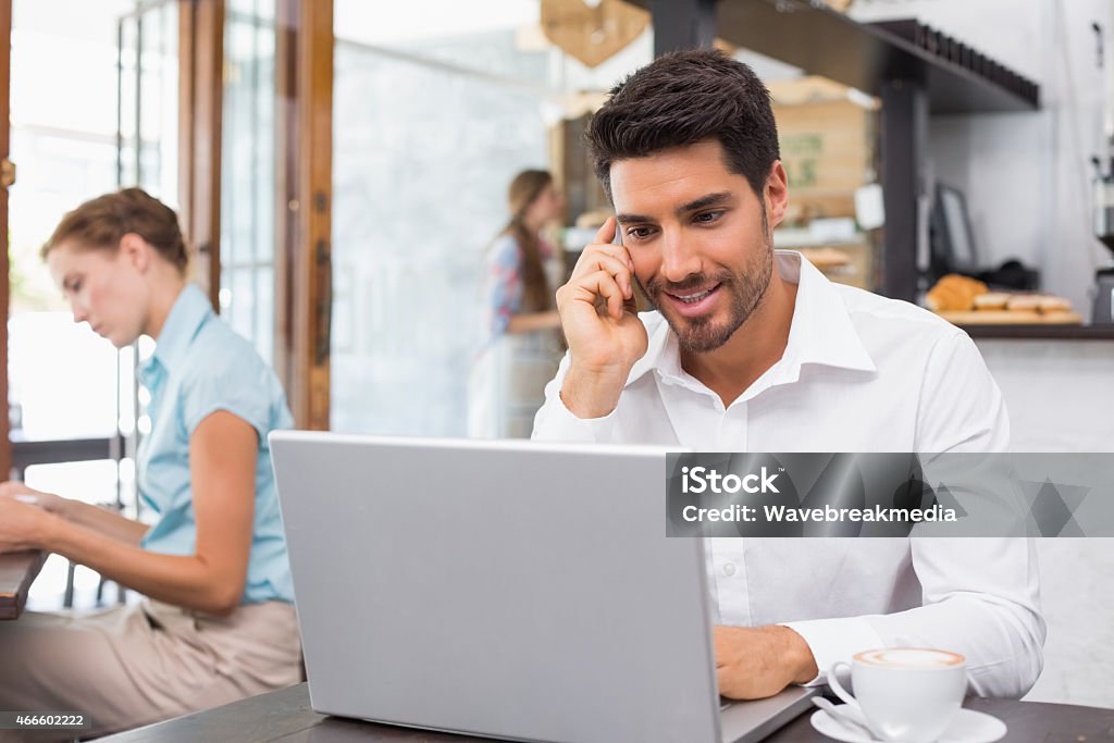 Man using laptop and mobile phone in coffee shop Portrait of a happy young man using laptop and mobile phone in the coffee shop 20-24 Years Stock Photo