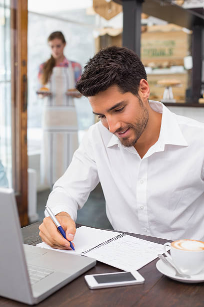 istock Man writing notes with laptop in coffee shop 466602680