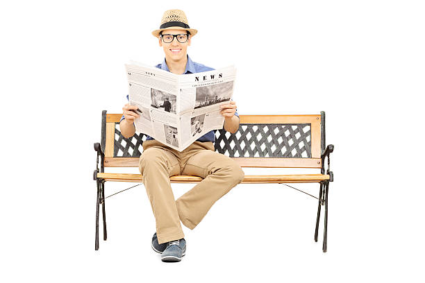 istock Young man seated on a wooden bench holding newspaper 466604217