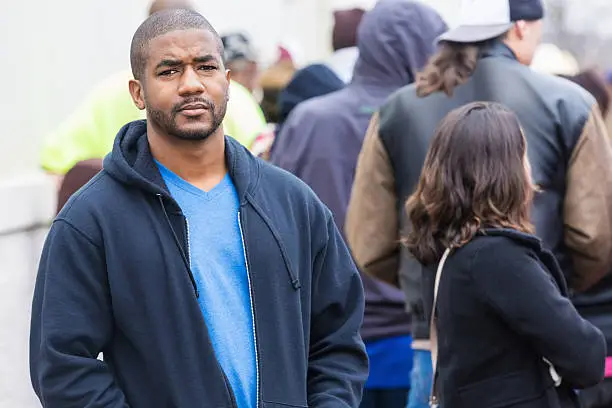 Photo of Serious man standing outside on crowded city sidewalk