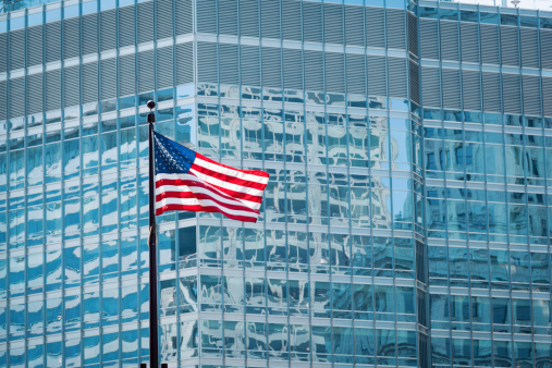 Subject: U.S. Flags in front of skyscraper, a view of corporate America with its finance, business and industry.