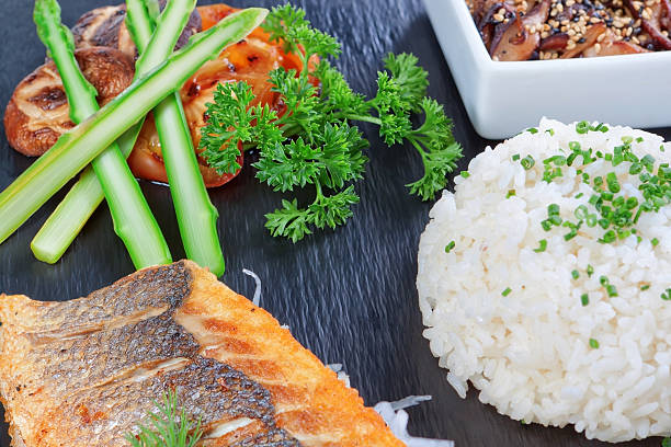 A delicious piece of fish on a background of greens, rice and mushrooms. Sushi dishes.