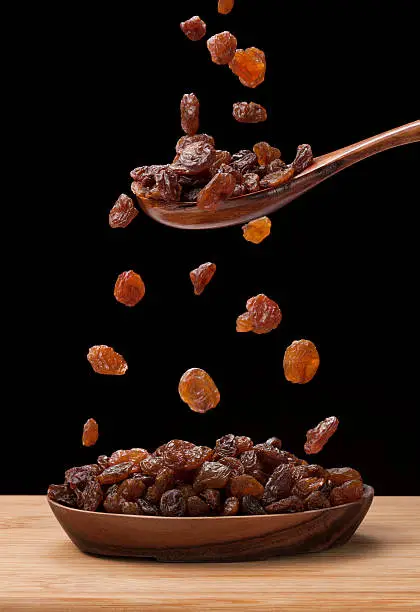 Raisin is flowing in wooden bovl photographed on black background