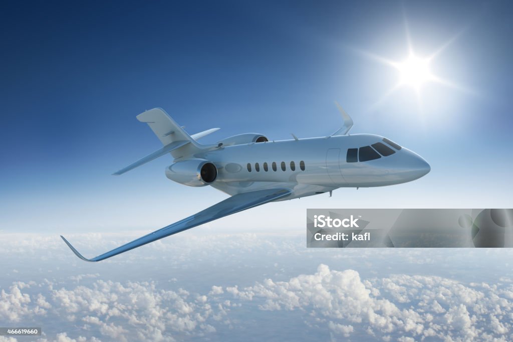 Private jet flying past sun in blue sky Private jet flies past sun - in blue sky above the clouds Corporate Jet Stock Photo