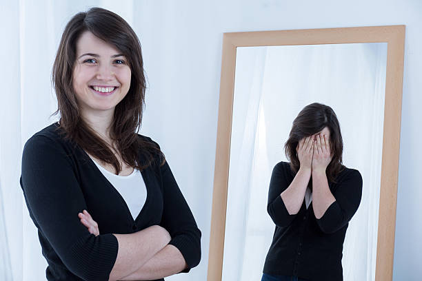 Woman smiling while reflection has hands over face  Young pretty woman pretending to be happy imitation stock pictures, royalty-free photos & images