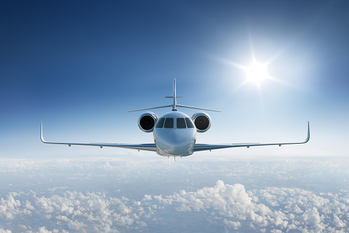 Private jet flies towards the camera in blue sky above the clouds