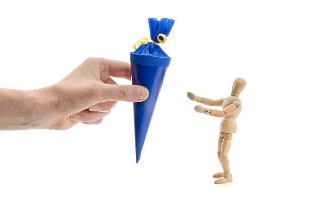wooden mannequin gets a conical bag of sweets conical bag of sweets. This "bags" are typical german, the children get them at the last day in kindergarden or /and the first day in school. They are sweets and goodies inside. zuckertüte stock pictures, royalty-free photos & images