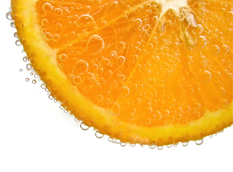 Close-up of half orange fruit in water against white background.