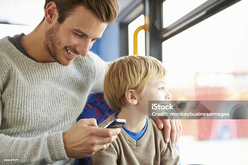 Father Using Mobile Phone On Bus Journey With Son Happy Smiling Father Using Mobile Phone On Bus Journey With Son Bus Stock Photo