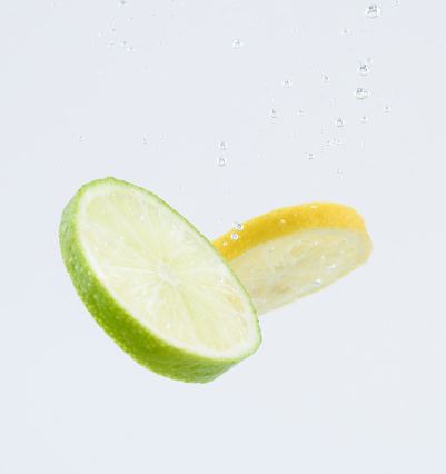 Fresh Fruit Dropping in Water - Lemon and lime splashing in water.  Studio image on white.