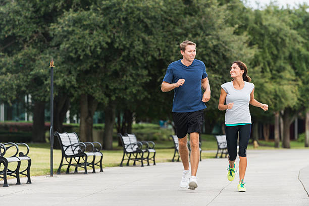 Front view of mature couple jogging or power walking together along a pedestrian walkway in a park.  Trees and benches line their path.